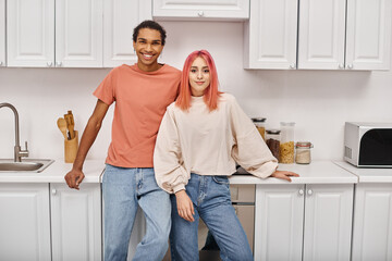 joyful attractive multicultural couple in comfy attire posing together and smiling at camera