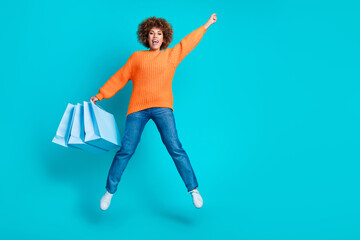 Full body portrait of carefree pretty lady hold store bags jump raise fist empty space isolated on...