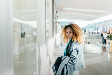 A young black girl walking between stores in a shopping center window shopping. Look at camera. White background with slight overexposure