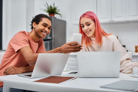 happy loving multiracial couple in casual attires working at laptops and looking at smartphone