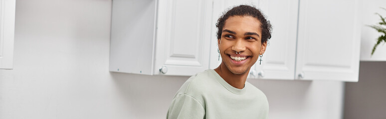 good looking cheerful african american man in green sweater looking away while in kitchen, banner