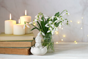 little Buddha figurine, Snowdrop flowers, books and candles on table close up. spring season. esoteric spiritual practice for Relaxation, harmony soul, meditation, life balance
