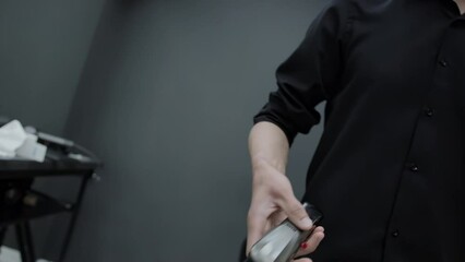 A man in a black shirt rotates and tosses a hair clipper in his hand. The concept of fashionable and stylish haircuts in a barbershop. Slow motion