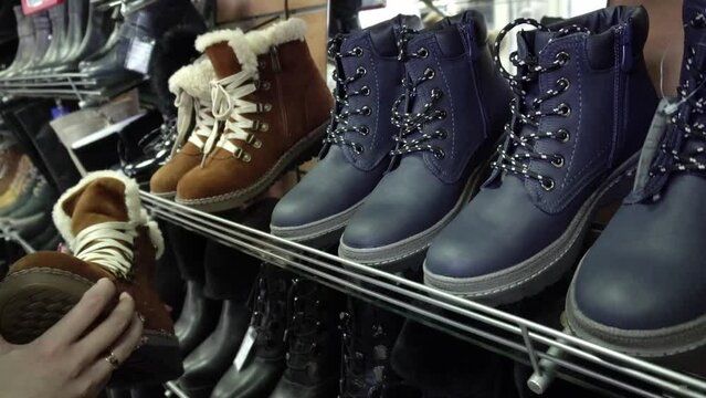 Selection of spring and autumn shoes in a store on display. Hands of a girl with manicure holding shoes, sale