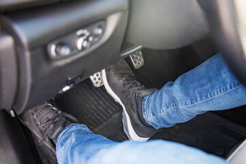 man's feet in black sneakers on the floor in a car pushing down the brake pedal, carefully driving car, waiting on the traffic light concept