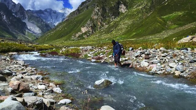 Man hiking on beautiful Pin bhabha pass trail crossing through Glacial river in Himalayas mountains with backpack. Travel Lifestyle wanderlust concept