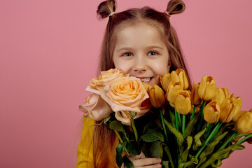 Little smiling girl holding flowers on pink background. International women's day.