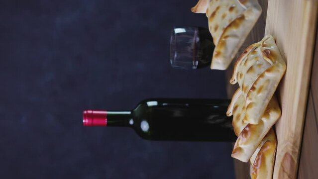 Chilean wine glasses and bottle and empanadas variety. Chile Food background. Fresh ingredients on wood. Selective Focus, vertical video