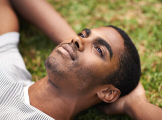 African man, thinking and relax on grass in nature, idea and vision on summer holiday plan. Thoughtful, enjoying fresh air or reflection, sunshine and peace for freedom after work week on vacation