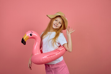 Redhead teen girl with flamingo pool float toy wearing hat on pink background. Summer, vacation