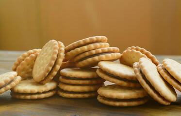 A round sandwich cookie with coconut filling lies in large quantities on a brown wooden surface....