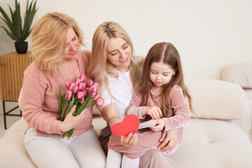 Happy Women's Day! The child's daughter congratulates her mother and grandmother, giving them flowers tulips. Grandmother, mother and girl smile and hug. Family holiday and unity.