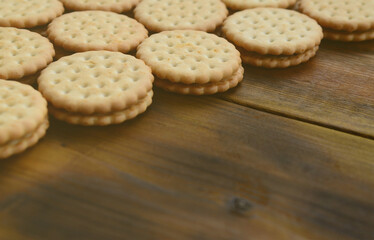 A round sandwich cookie with coconut filling lies in large quantities on a brown wooden surface. Photo of edible treats on a wooden background with copy space.