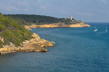 Fonda beach (Cala Fonda) and La Marquesa pine forest with the Mora tower and the cliffs in the background in a sunny day. Tarragona, Catalonia, Spain. - obrazy, fototapety, plakaty