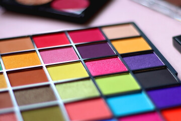Various colorful eyeshadow palettes on bright pink background. Selective focus.
