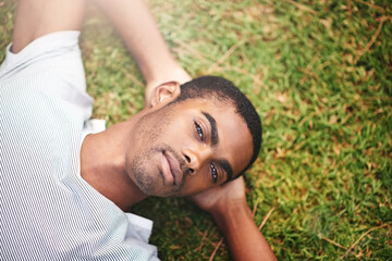 Portrait, peace and black man on grass in garden of summer for wellness or mindfulness. Face, relax and sunshine with confident young person lying in green field from above for break or rest