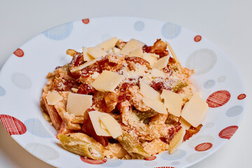 a portion of pasta with vegetables, parmesan and bacon in a plate.