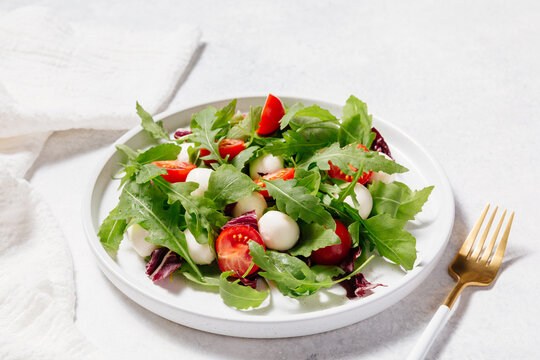 Fresh green salad made with mozzarella cheese, cherry tomatoes, arugula and olive oil on white stone table background. Healthy food and diet concept. Flat lay, copy space - Powered by Adobe