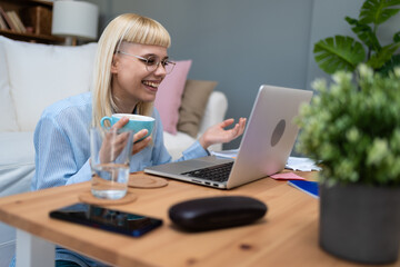 Young business woman freelance expatriate financial and digital marketing expert in smart casual working at home in home office taking a break with coffee and video call with friend or colleague