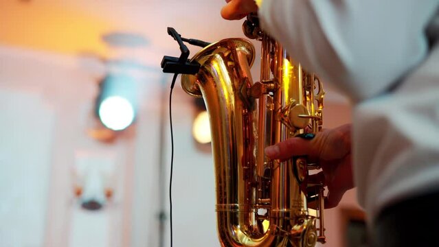 A male saxophonist plays music at an indoor concert at a festival with light and music. A golden saxophone is in the hands of a man. Slow mo