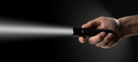Black flashlight in human hands on a black background, including a white beam