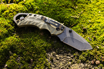 Tactical folding knife for survival on moss background