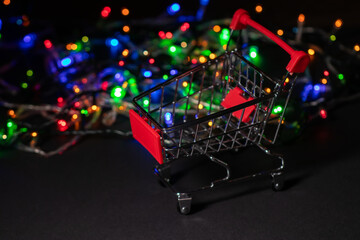 New year shopping. Shopping cart on Christmas garland light background.