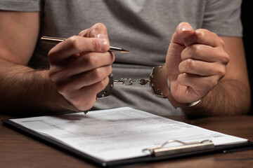 Tax evasion, crime and fraud concept. Man in handcuffs filling out tax form Income tax return...