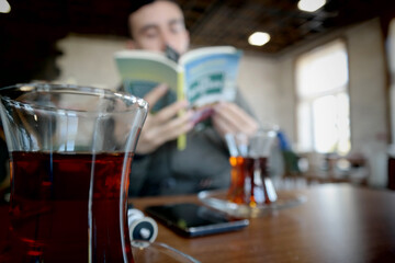 A male student reading a book with tea in a cafe.