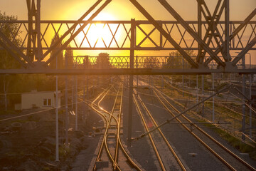 Kolorowy zachód słońca nad torami kolejowymi w Ostrowcu. Konstrukcje metalowe i tory kolejowe zanurzone w złotych promieniach zachodzącego słońca w majowy wieczór.