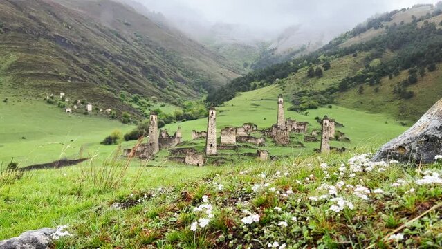 View of the medieval Targim tower complex in the Caucasus mountains surrounded by greenery. The Caucasus Mountains on a cloudy day in Ingushetia. Russia, 4K.