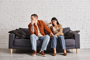 young interracial couple in quarrel sitting on couch in living room at home, divorce concept