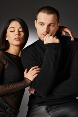 sensual asian woman embracing handsome man in black attire sitting on grey backdrop with light