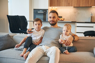 Conception of relaxation. Father with two baby boys is sitting at sofa