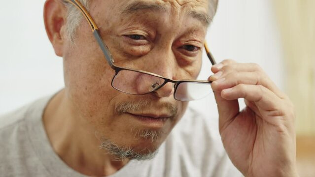 Footage handheld close up shot, Face of Mature man wearing eyeglasses sitting on sofa in living room for relaxation, then he take off glasses and looking forward and smile