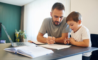 Writing the homework. Father and son are at home by the table