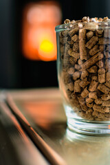 Pellet for stove or boiler in a glass, compressed wood pellet with a stove in background