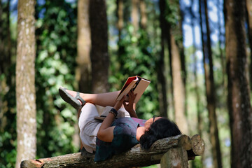 A woman reading a book while lying on a wooden bench