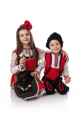 Bulgarian girl and boy in ethnic folklore costumes with spring traditional martenitsa on hands and bouquet of snowdrops, happy Baba Marta day, Bulgaria - 748733251