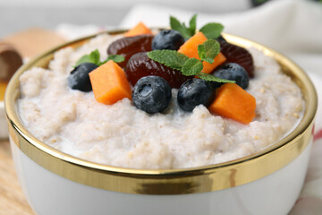 Delicious barley porridge with blueberries, pumpkin, dates and mint in bowl on table, closeup