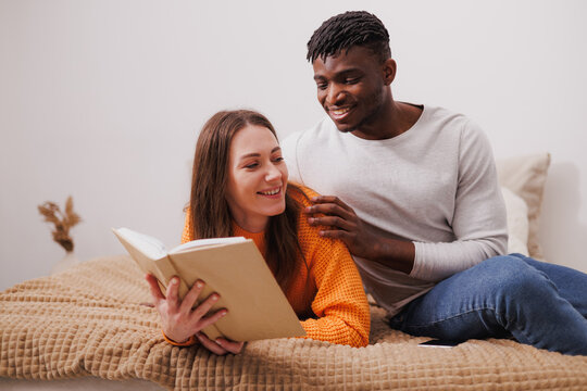 Smiling african american man hugging girlfriend reading book at home