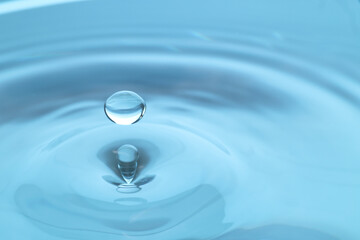 Naklejka na ściany i meble Drop falling into clear water on light blue background, closeup