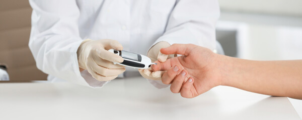 Obraz na płótnie Canvas Endocrinologist checking patient's blood sugar level with digital glucometer at table, closeup. Banner design