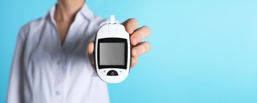 Endocrinologist holding digital glucometer on light blue background, closeup. Banner design with space for text