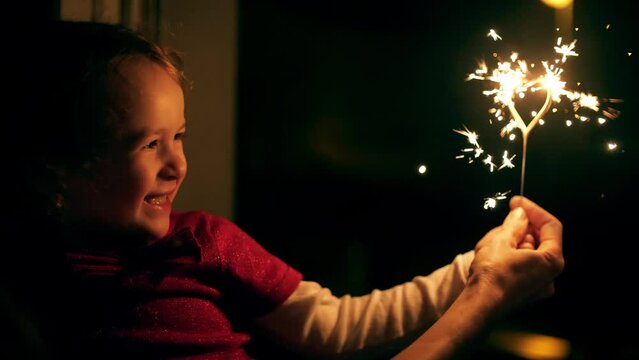 Smiling girl and her mom with a heart shaped sparkler in the evening. Family holiday or birthday concept