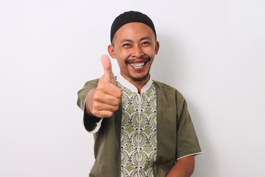 A smiling Indonesian Muslim man in koko and peci gives a thumbs-up gesture, expressing satisfaction or approval. Isolated on a white background