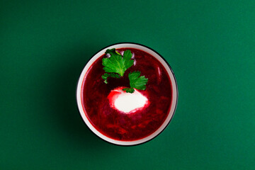 red beet soup in a bowl with parsley and sour cream in a bowl on a green background. top view. Bowl...