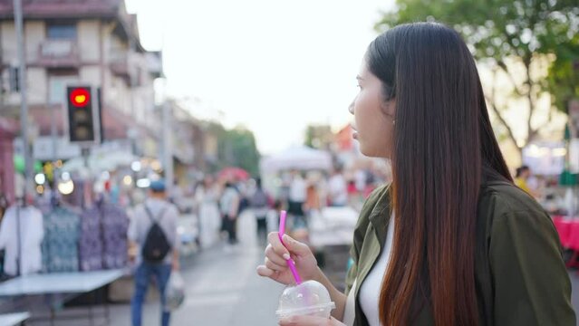 Happy Asian woman enjoy and fun outdoor lifestyle travel in Thailand on summer holiday vacation. Attractive girl walking and shopping at weekend street market and eating street food in Chiang Mai city