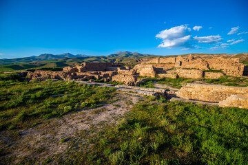Fototapeta na wymiar Sunlit Remnants of the Takht-e Soleyman Fortress Amidst Rolling Hills in West Azerbaijan Province, Iran