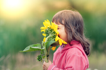 Little girl outdoors smelling sunflower